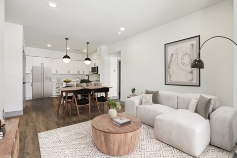A modern living room with a grey sofa, wooden coffee table, and a dining table with chairs.