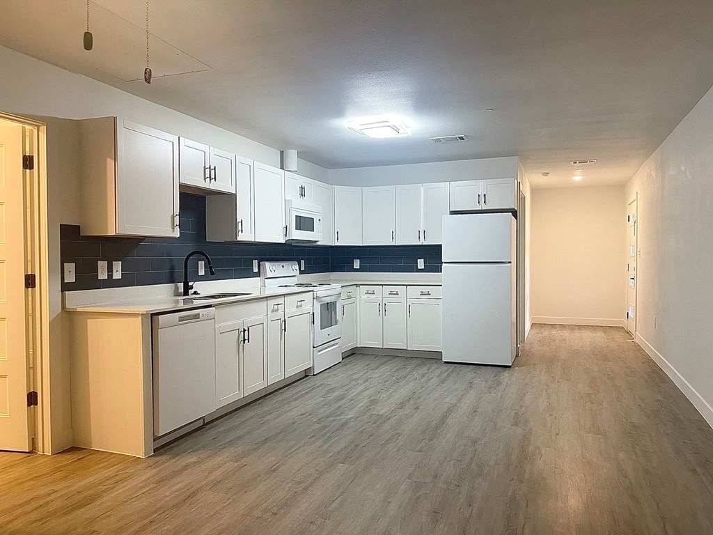 an empty kitchen with white cabinets and appliances and wood floors