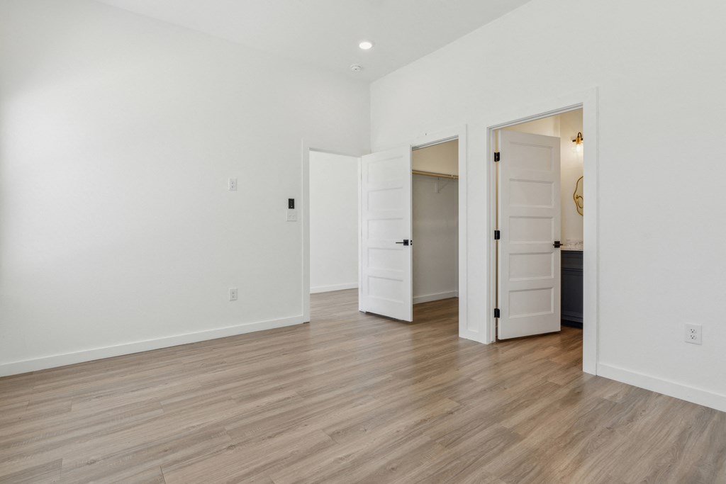 A white room with a wooden floor and three open doors.