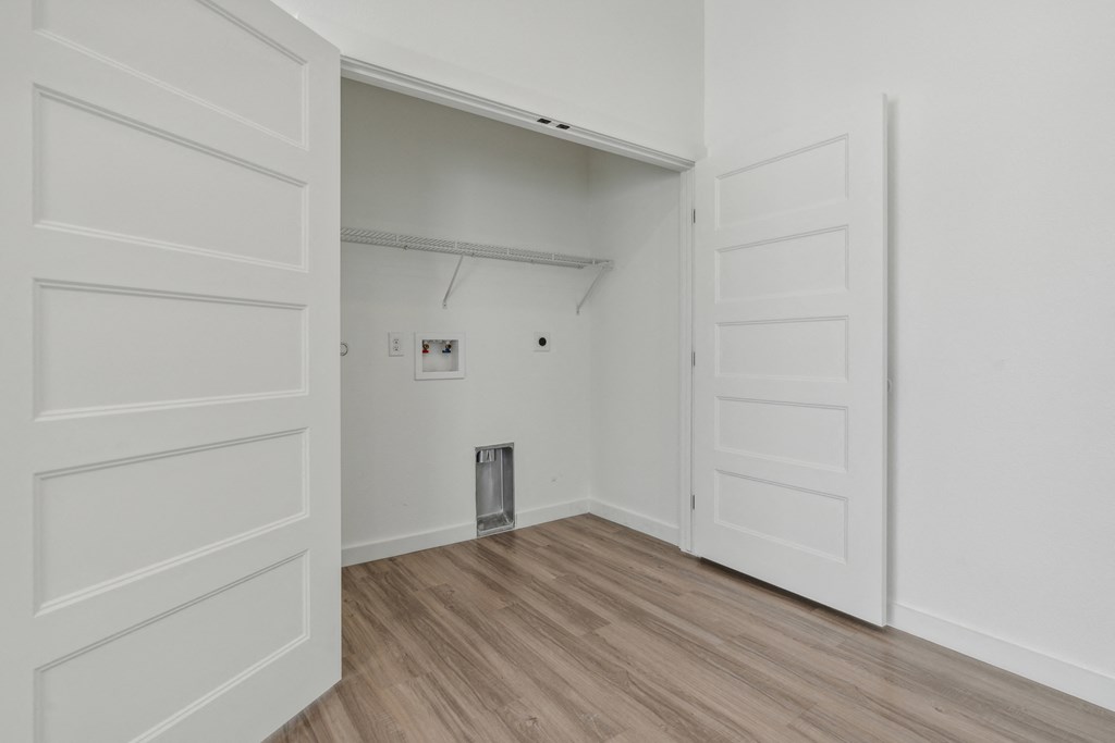A white door is open to a room with a wooden floor and a metal trash can.