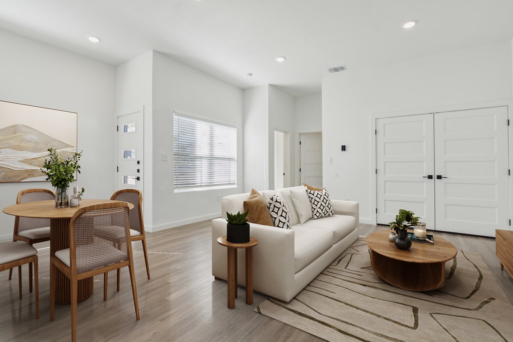 A modern living room with a white sofa, wooden coffee table, and a dining table with chairs.