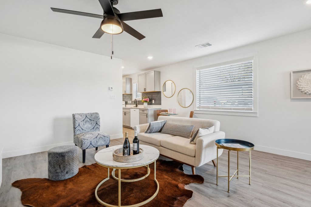 A living room with a white couch, a grey armchair, a round table with a bottle on it, and a brown cowhide rug.