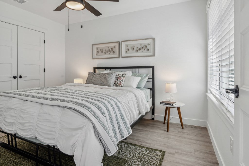 A bedroom with a bed, a ceiling fan, and two lamps.