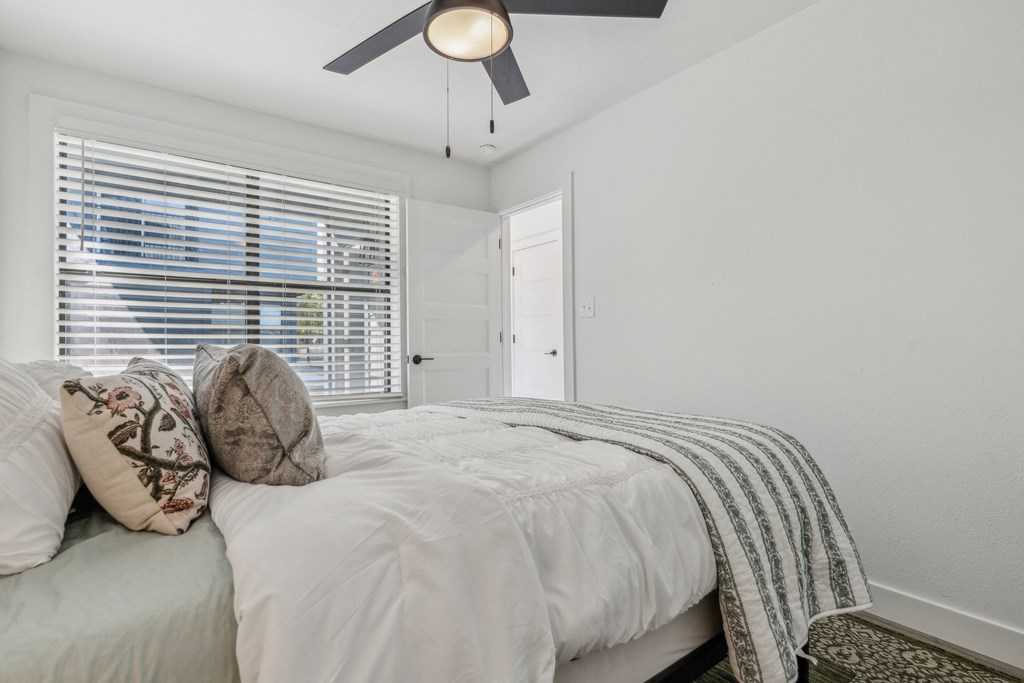 A bedroom with a bed, pillows, and a ceiling fan.