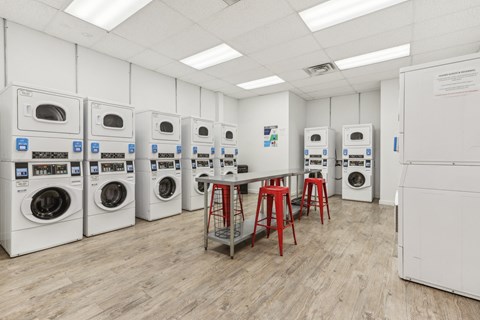 a laundry room with a row of washing machines and red stools