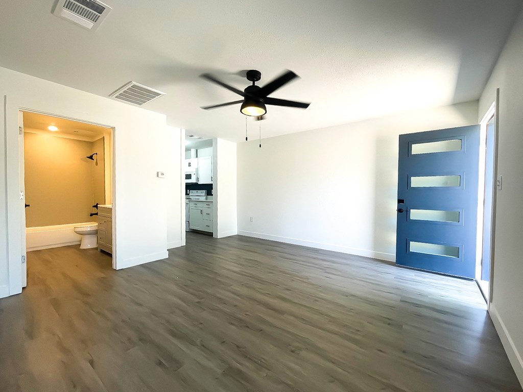 an empty living room with a ceiling fan and a blue door
