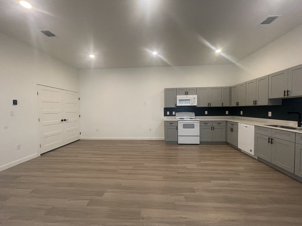 an empty kitchen with white cabinets and a wooden floor