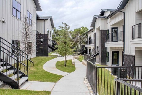 A white building with a black railing and a tree in front.