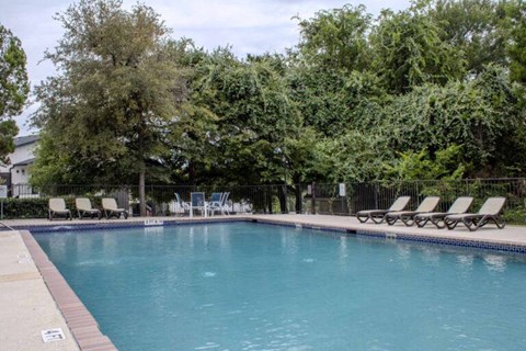 A pool surrounded by trees and lounge chairs.