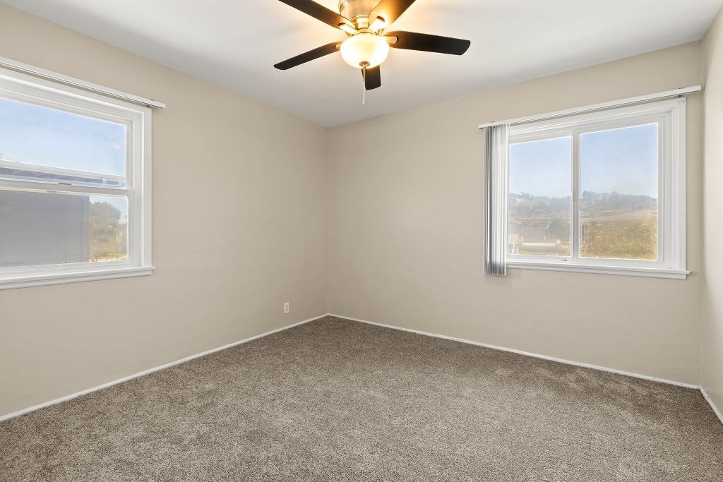 A room with a ceiling fan and two windows.