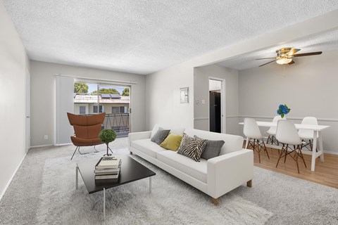 A living room with a white couch, a brown chair, and a glass table with a plant on it.