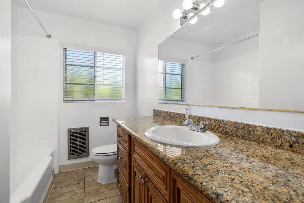 Apartments for Rent in Van Nuys CA - Colonial Manor - White Bathroom with Tub, Toilet, Granite Sandy Vanity, Mirror, and Tan Cabinetry