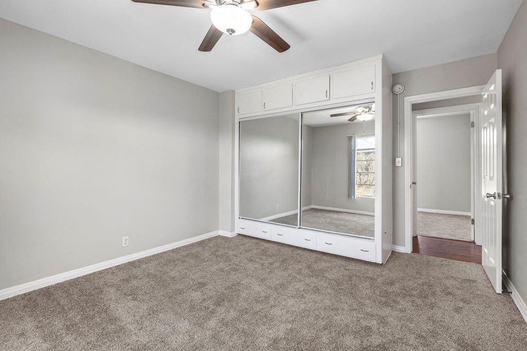 Van Nuys CA Apartments - Colonial Manor - Spacious Bedroom Area, Unfurnished, with Carpeted Floors, Sliding Mirror Closet, White Walls, Ceiling Fan, and Lights