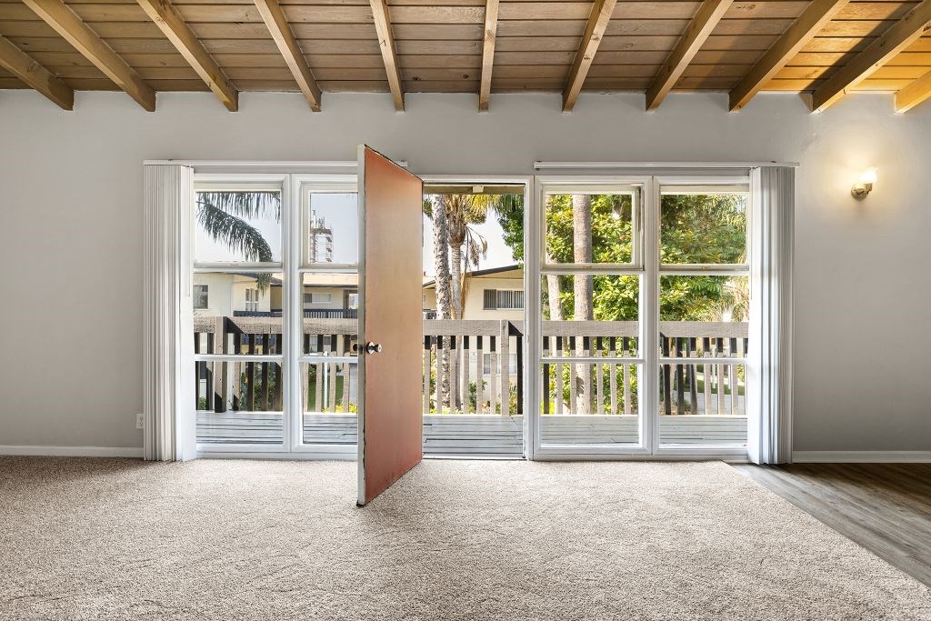A room with a carpeted floor and a wooden ceiling with a door open to a balcony.
