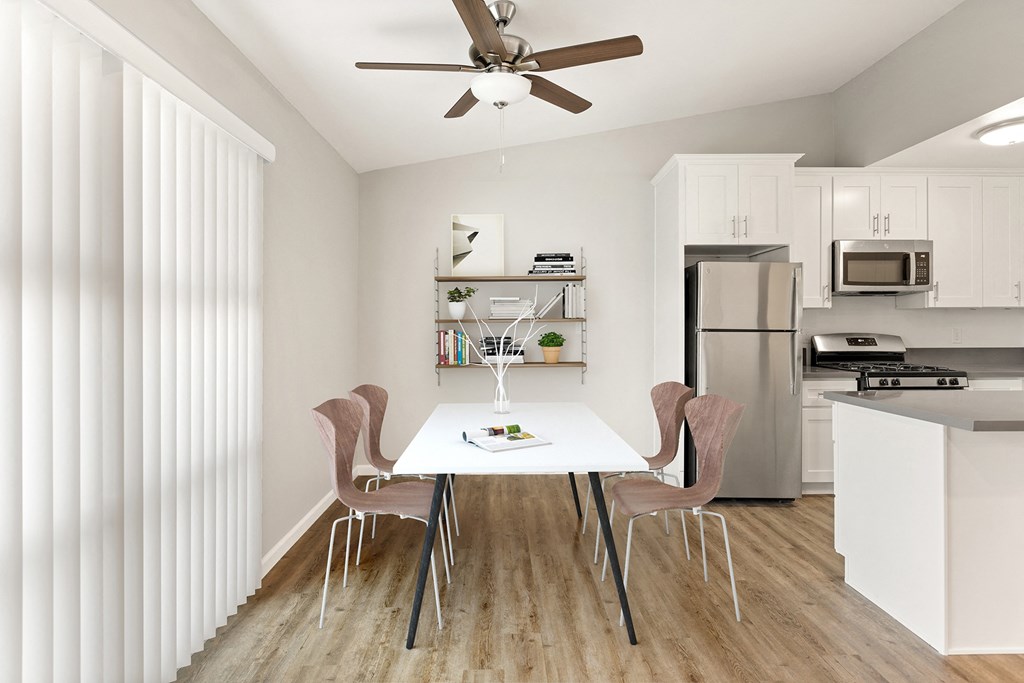 a dining room with a white table and chairs and a kitchen with stainless steel appliances