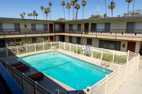 A pool surrounded by a white fence and red lounge chairs.