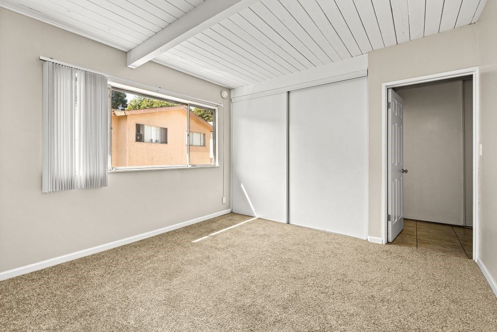 A room with a carpeted floor and a window showing a building outside.