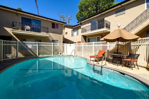 A swimming pool in a residential area with a sun umbrella and chairs.