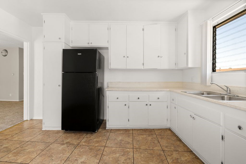 A black refrigerator sits in a kitchen with white cabinets.