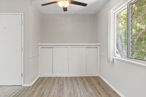 A room with a ceiling fan and a window with a view of trees.