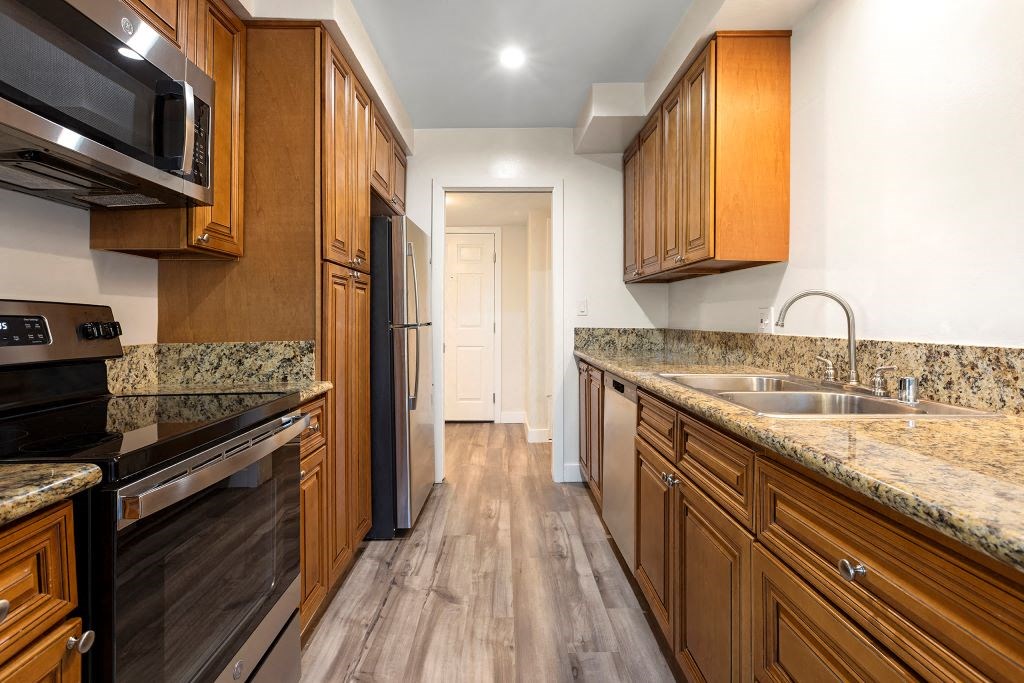 Encino CA Apartments - White Oak Terrace - Interior View Of Kitchen Featuring Brown Wooden Cabinetry and Stainless Steel Refrigerator, Oven Stove, and Microwave With Beige Granite Countertop