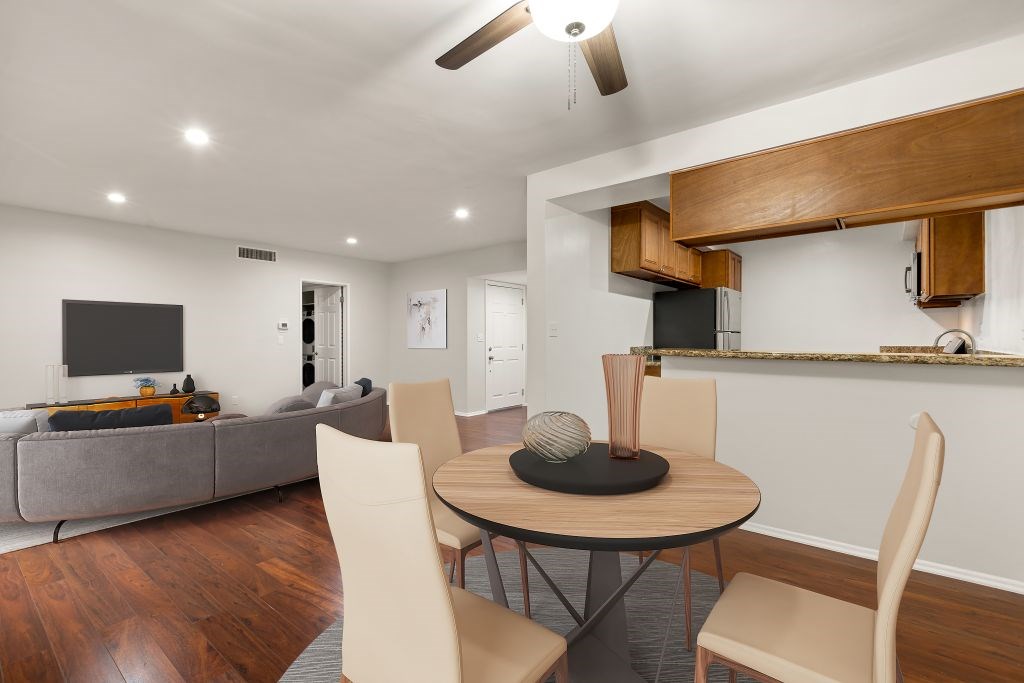 A modern living room with a grey sofa, a wooden dining table and chairs, and a kitchen area with a wooden countertop.