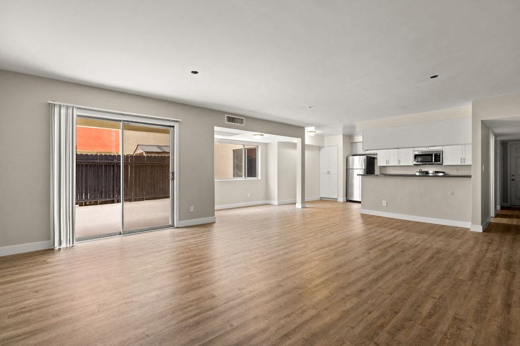 an empty living room with a sliding glass door and a kitchen in the background