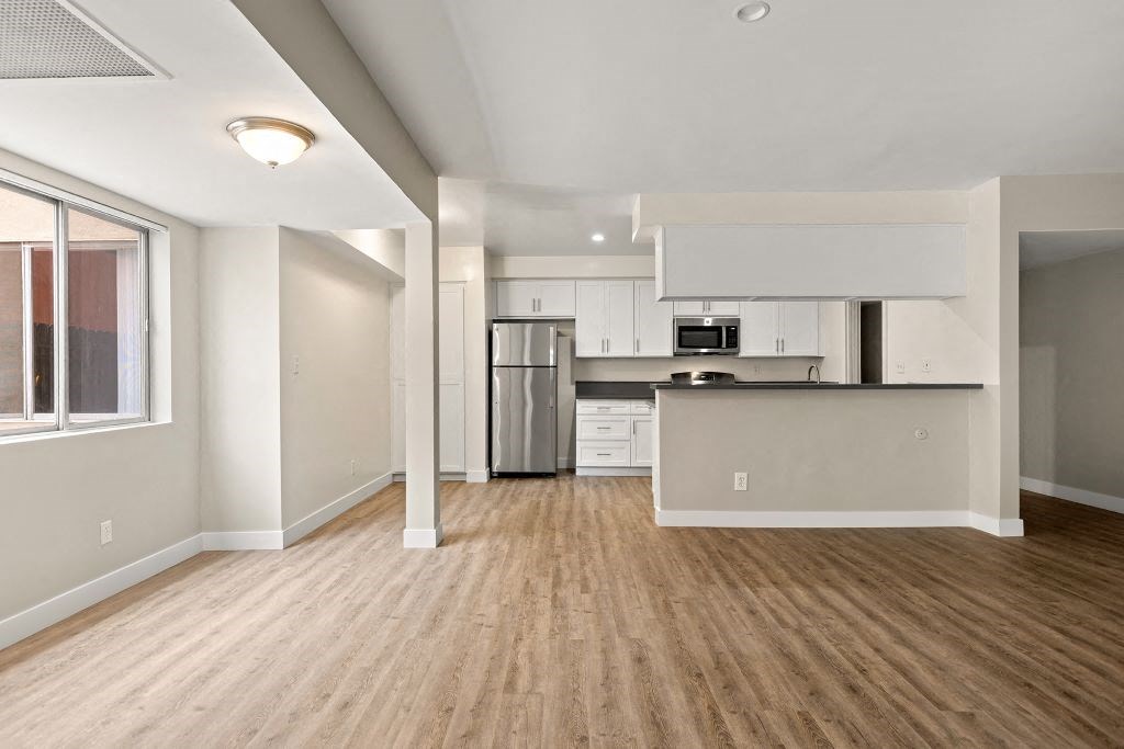 an empty living room with a kitchen in the background