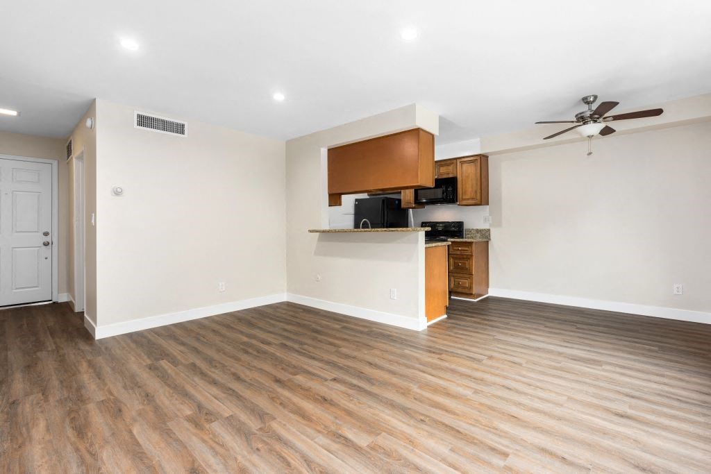 an empty living room with a kitchen in the background