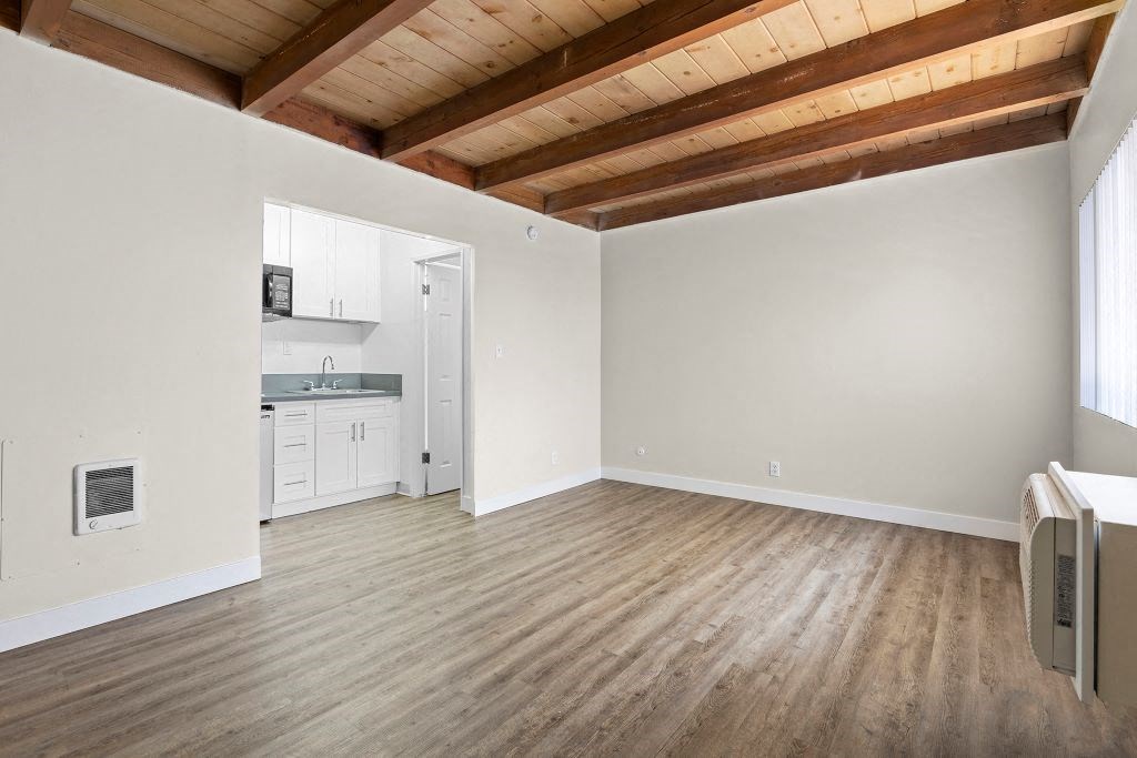 an empty living room with a kitchen in the background
