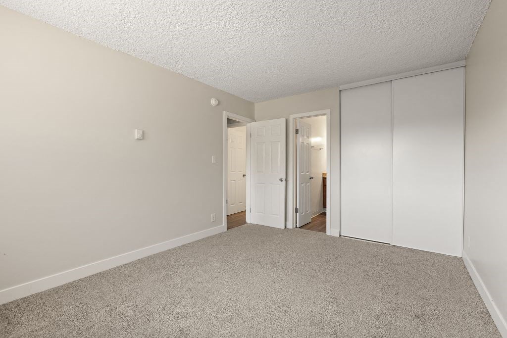 a bedroom with white walls and carpet and a door to a closet