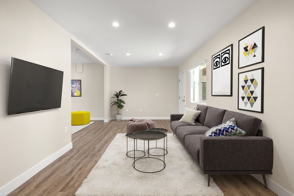 A living room with a grey couch and a black TV on the wall.