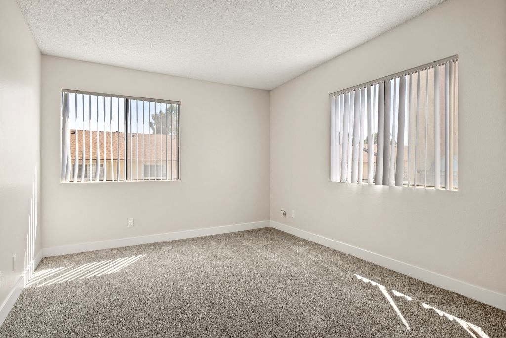an empty living room with two windows and carpeting