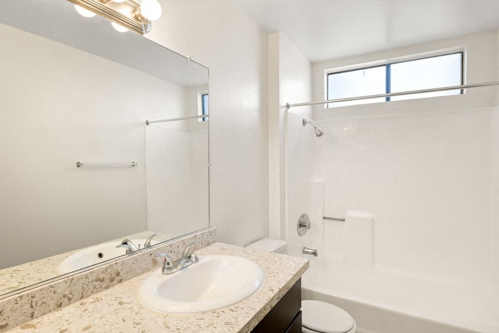 A white bathroom with a sink, mirror, toilet, and bathtub.
