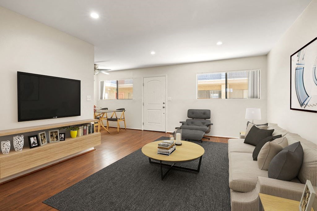 A living room with a grey couch, a wooden coffee table, and a flat screen TV mounted on the wall.