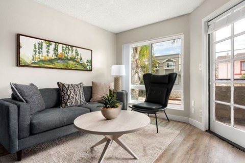 A living room with a grey couch, a white table, and a painting on the wall.