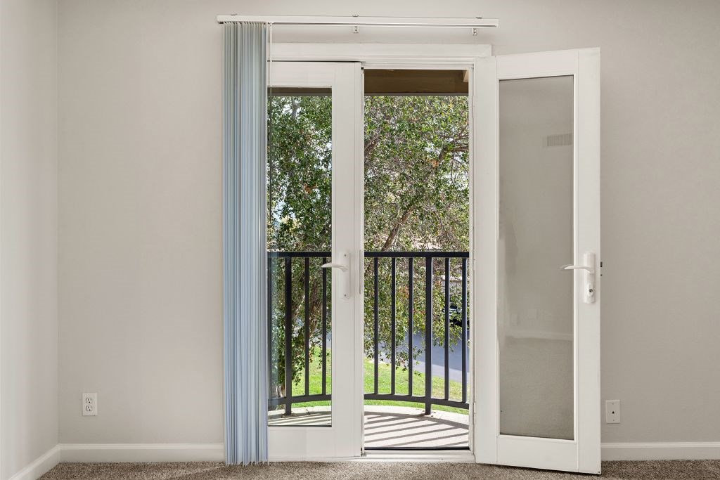A room with a white door and a balcony with a black railing.
