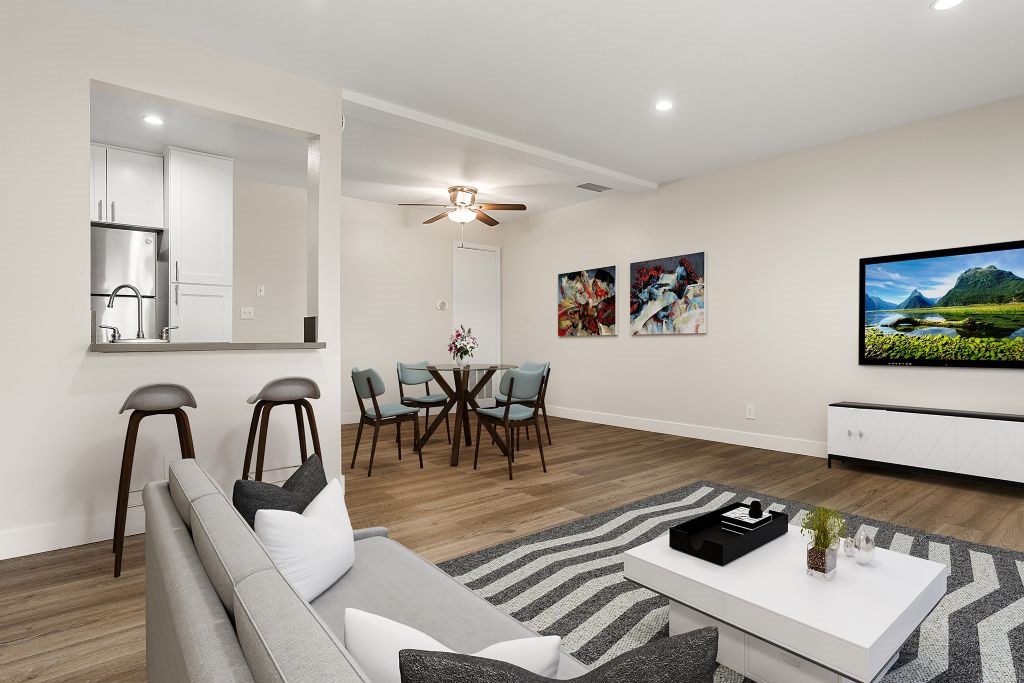 A modern living room with a grey sofa, a white coffee table, and a television on the wall.