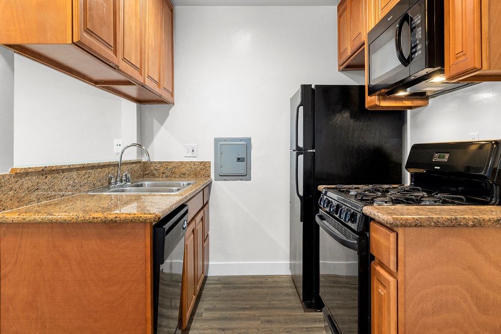 a kitchen with wooden cabinets and black appliances at Riverside Villas Apartments, Valley Village, California
