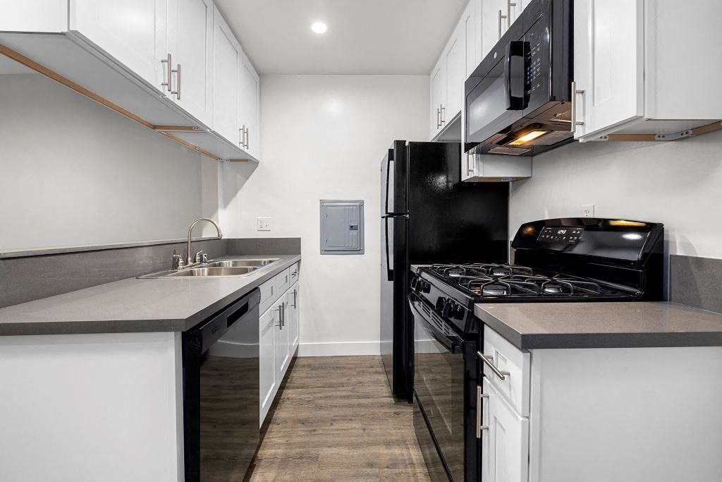 a kitchen with white cabinets and black appliances at Riverside Villas Apartments, Valley Village, California
