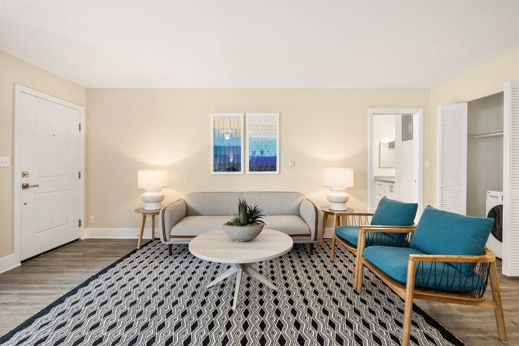 Living Room With Grey Couch, Diamond Shaped Black & White Area Rug, and Two Wooden Chairs at Casa De Marina Apartments, Los Angeles