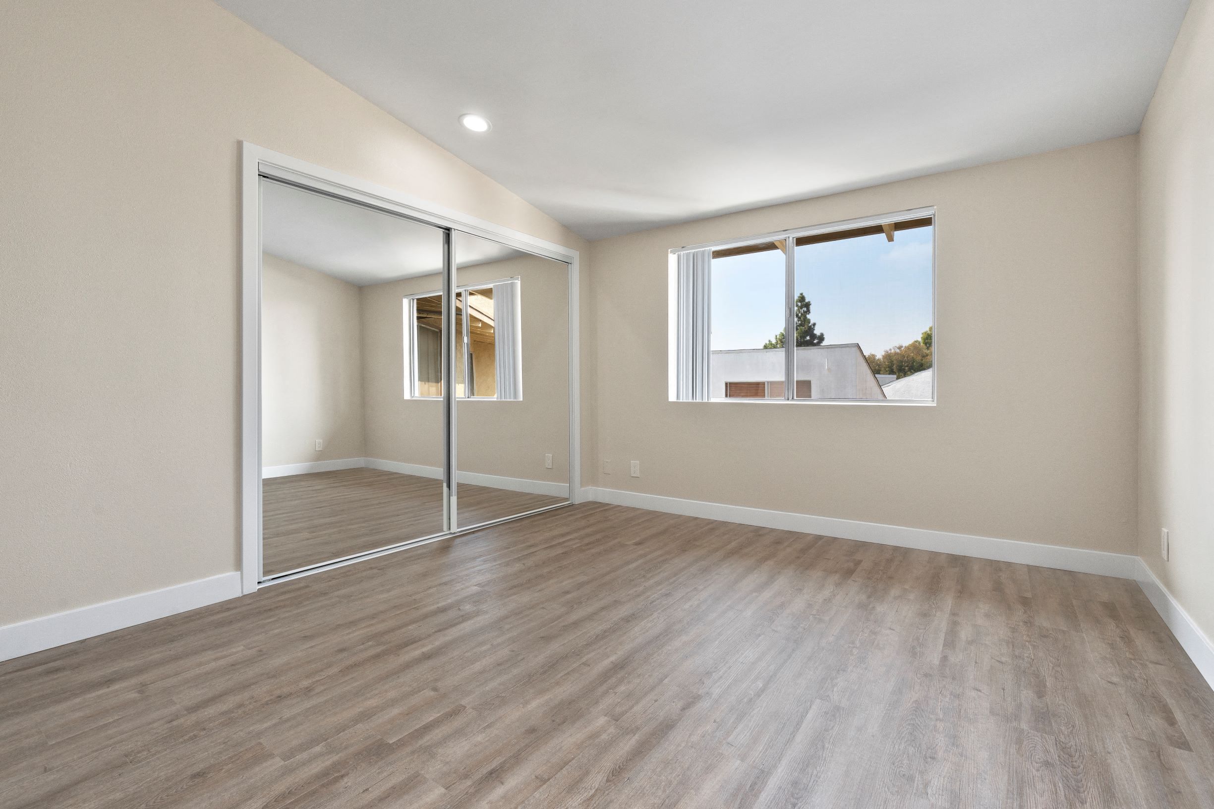 Apartments For Rent In Culver City, CA - Spacious Bedroom With Laminate Plank Flooring, A Large Closet With Mirror Sliding Doors, And A Window With Blinds.