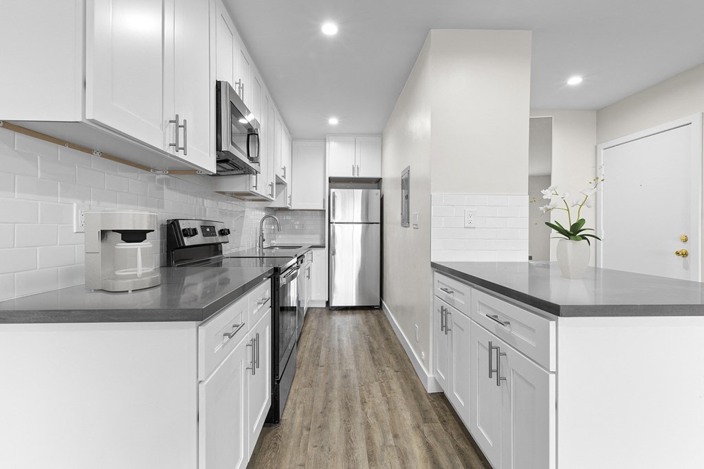 a white kitchen with white cabinets and black counter tops at Brookside Terrace Apartments, Encino California