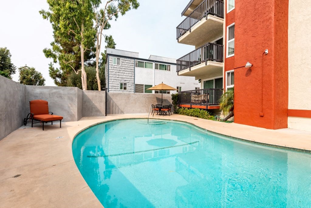 Culver City Apartments For Rent - Sparkling Pool With A Lounge Chair, Patio Set, And View Of Apartment Building.