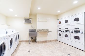 A laundry room with a washer and dryer on the left and a row of ovens on the right.