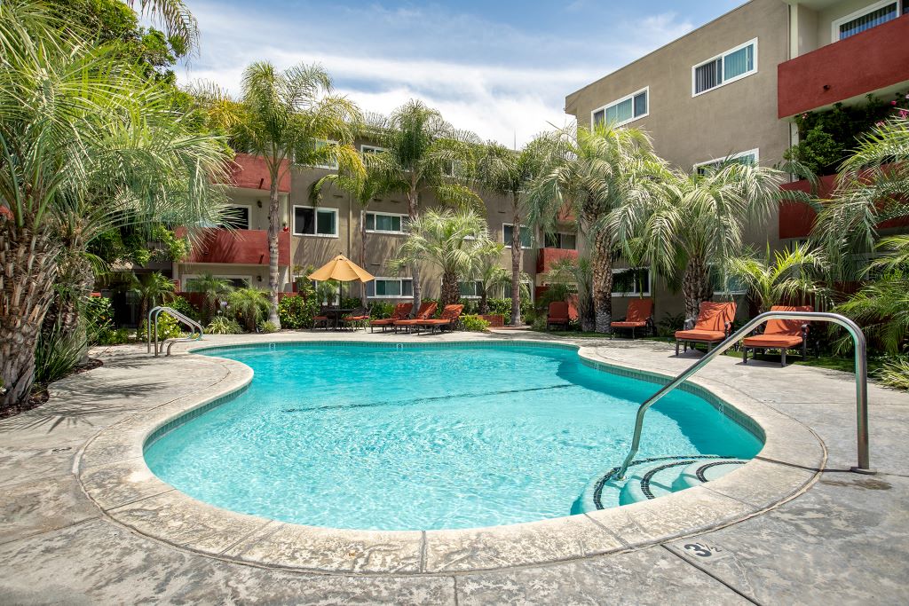 Woodland Hills Apartments - Sparkling Pool With Lounge Chairs, A Table With Umbrella, Palm Trees, And Lush Landscaping