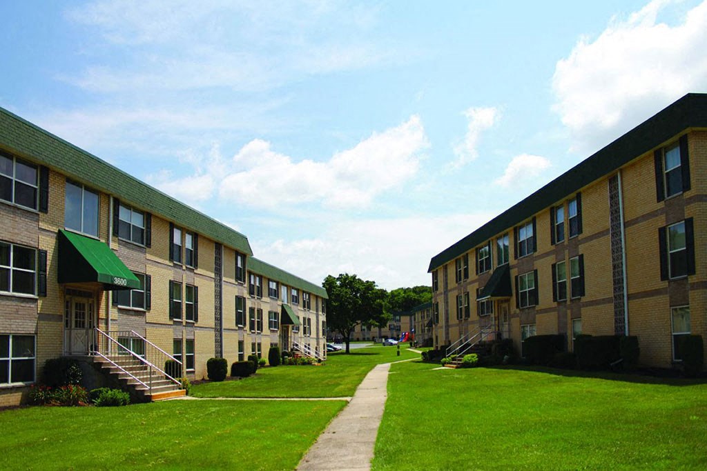 a row of brick apartment buildings with green grass and a sidewalk
