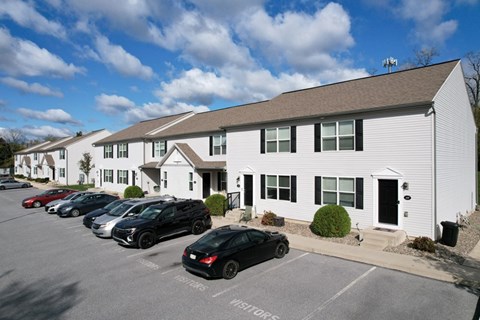 A parking lot with cars and a white building with a black door.