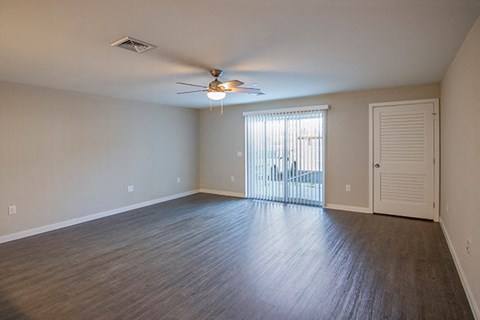 an empty living room with a ceiling fan and a door to a balcony
