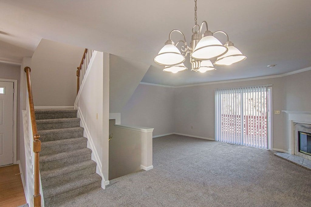 A living room with a grey carpet and a chandelier.